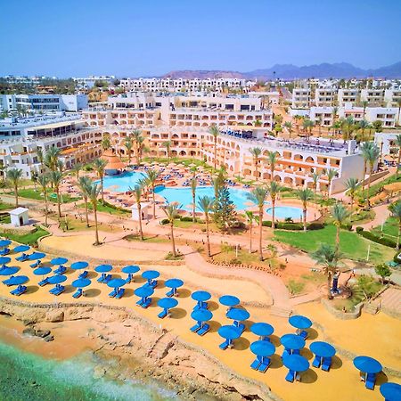 Pickalbatros Royal Grand Sharm - Adults Friendly 16 Years Plus Exteriér fotografie The photo shows a vibrant resort area with several buildings that appear to be accommodations or hotel units. There are multiple swimming pools surrounded by palm trees, creating a tropical atmosphere. In the foreground, there is a beach area with sa