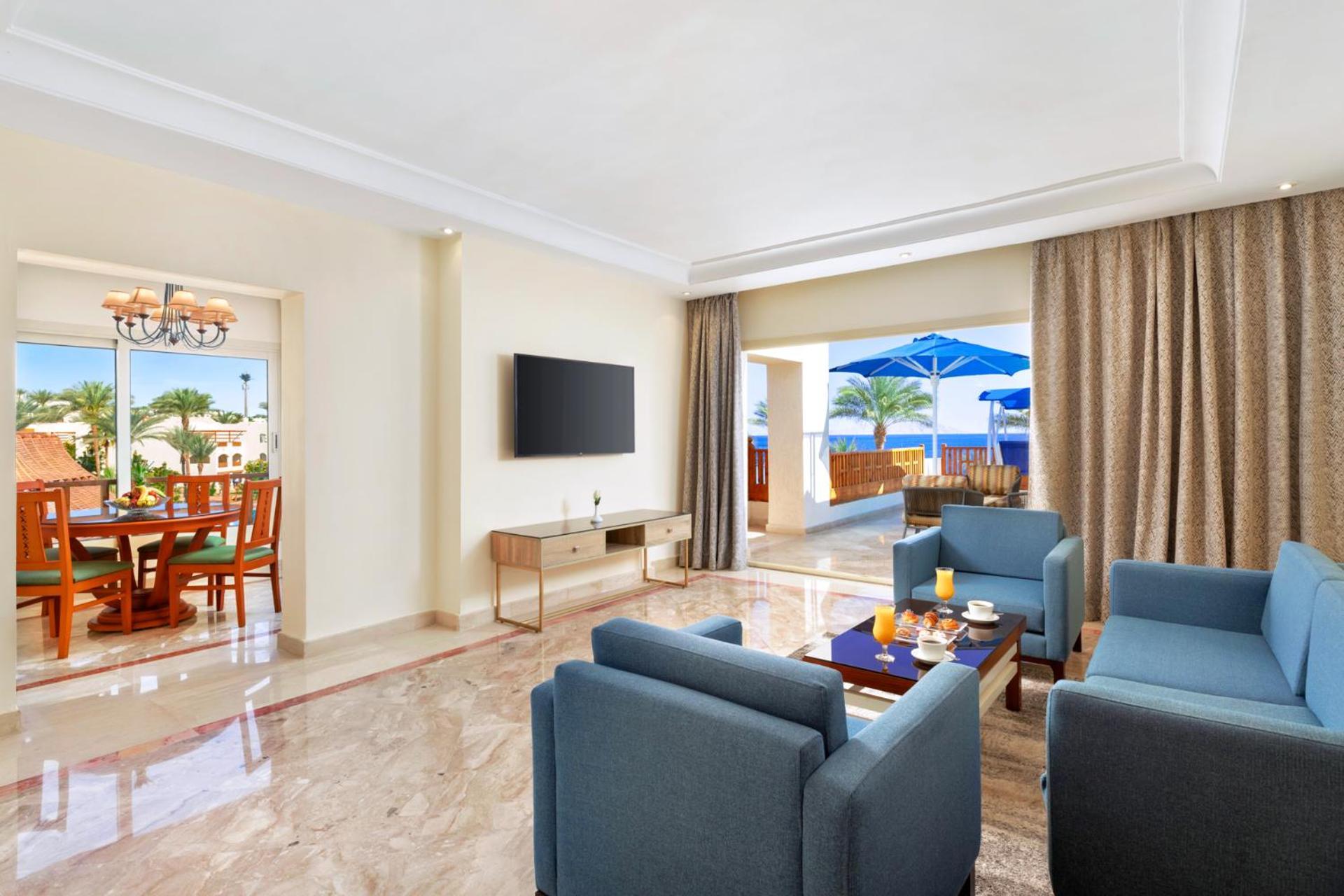 Pickalbatros Royal Grand Sharm - Adults Friendly 16 Years Plus Exteriér fotografie The photo shows a modern and spacious living area. There are several blue chairs arranged around a coffee table, which holds some refreshments. A large flat-screen TV is mounted on the wall, and there are sliding glass doors that open to an outdoor a