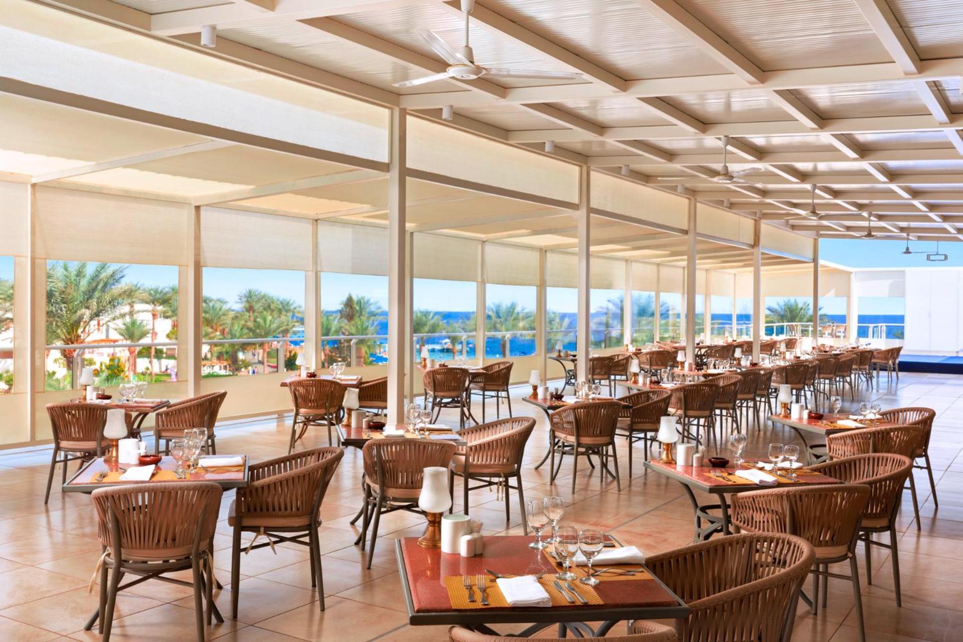 Pickalbatros Royal Grand Sharm - Adults Friendly 16 Years Plus Exteriér fotografie The photo shows a spacious dining area in a restaurant with a modern and airy design. It features numerous wooden tables set with glasses and cutlery, arranged in a way that gives an open feel. Large windows provide a view of the outside, showcasing 