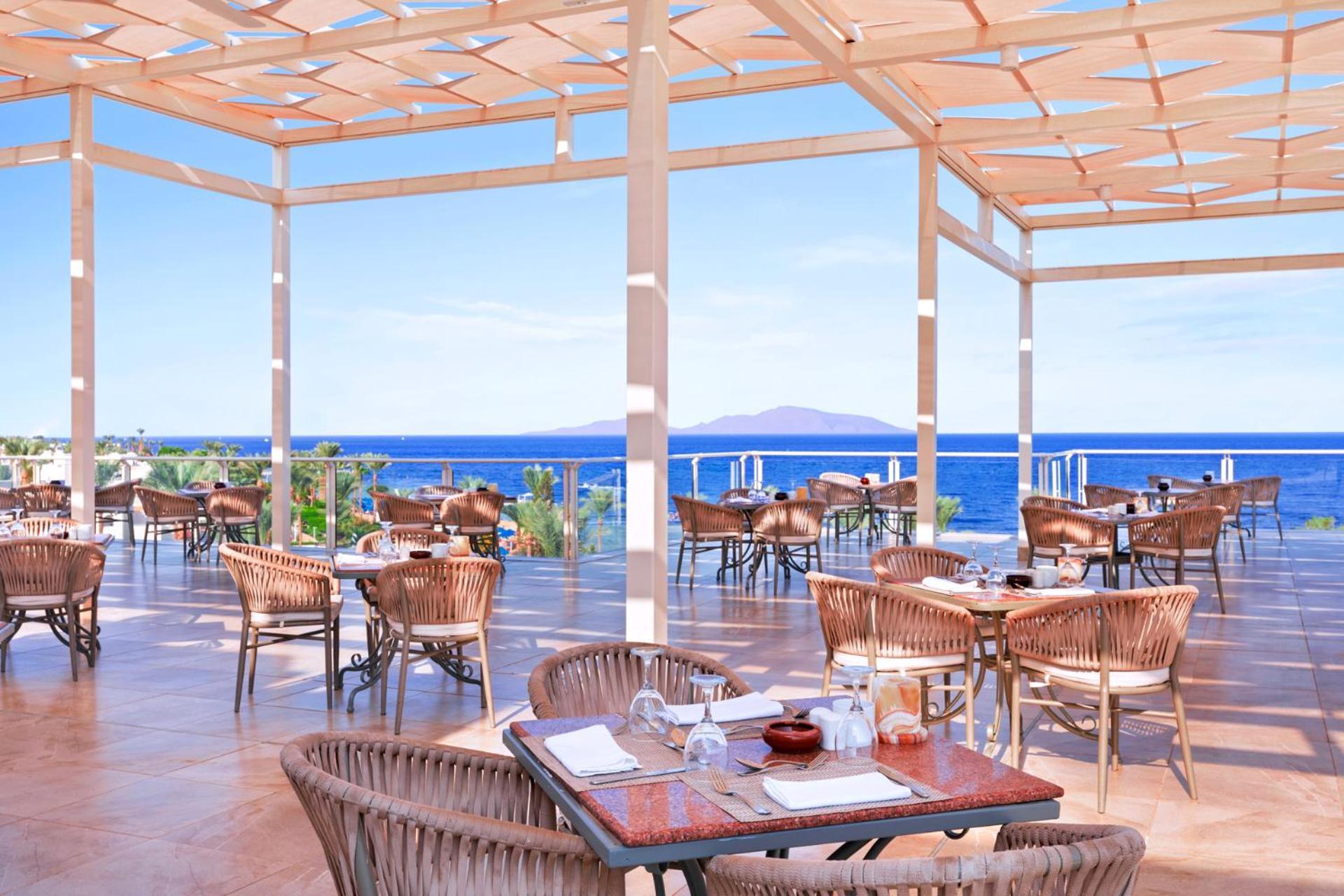 Pickalbatros Royal Grand Sharm - Adults Friendly 16 Years Plus Exteriér fotografie The photo shows a spacious outdoor restaurant with a beautiful view of the ocean. The seating area features several tables and wicker chairs. The open design includes a wooden pergola providing some shade, while large windows or openings allow for a 