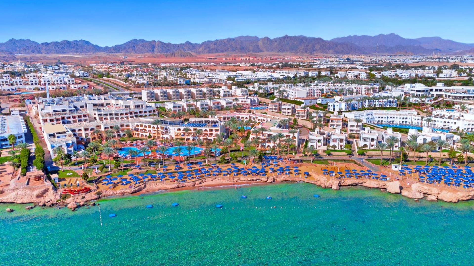 Pickalbatros Royal Grand Sharm - Adults Friendly 16 Years Plus Exteriér fotografie The photo shows an aerial view of a resort located by the coast. There are several swimming pools surrounded by sun loungers and umbrellas, as well as a beach area with clear turquoise water. In the background, there are multiple buildings of the res