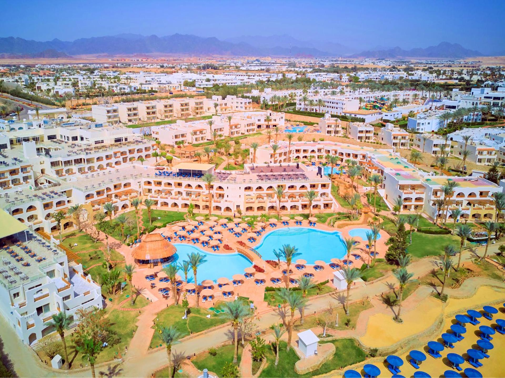 Pickalbatros Royal Grand Sharm - Adults Friendly 16 Years Plus Exteriér fotografie The photo shows an aerial view of a resort complex. There are several buildings arranged around a central area that features swimming pools. The pools are surrounded by palm trees and lounge chairs, indicating a tropical or sunny climate. In the back