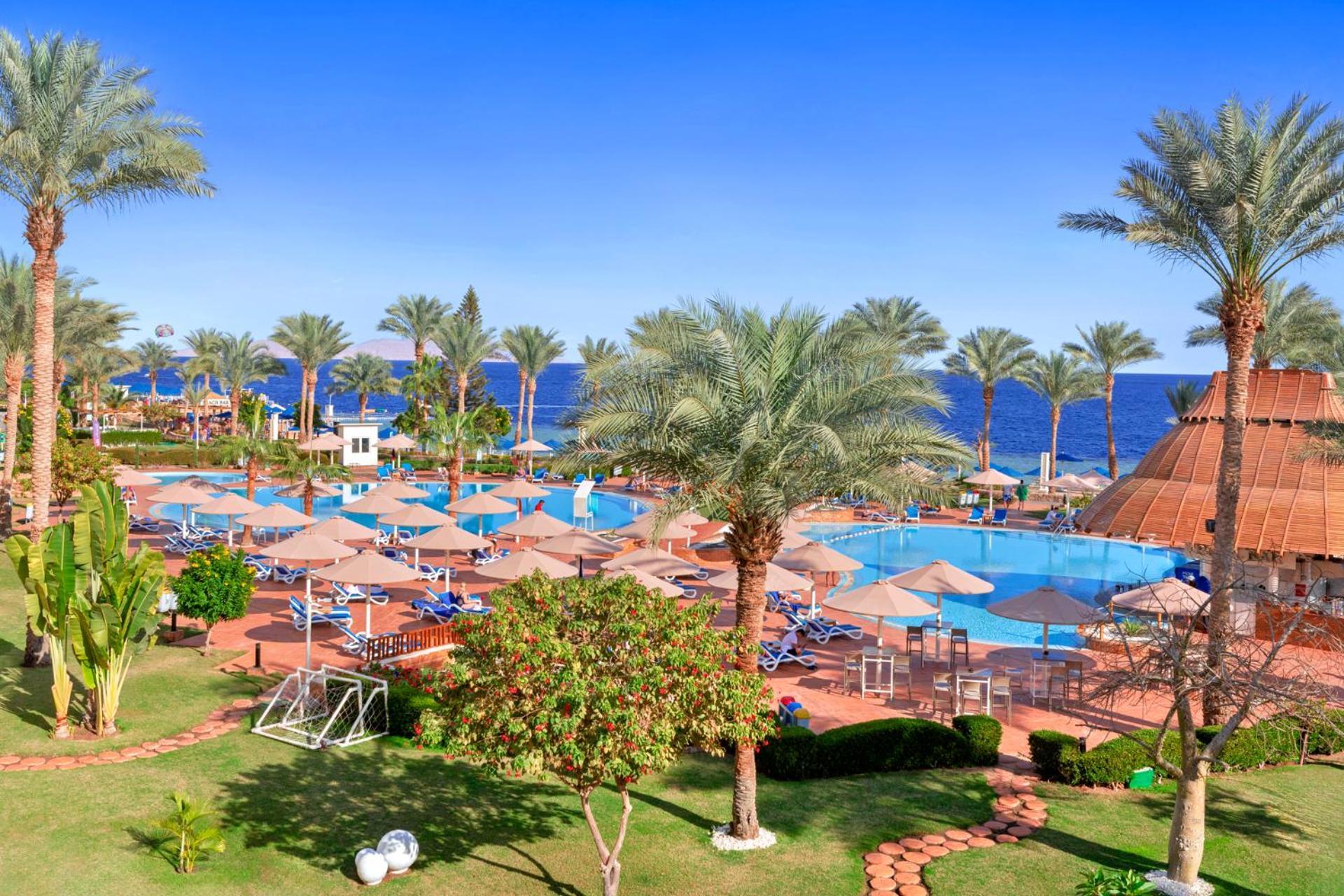 Pickalbatros Royal Grand Sharm - Adults Friendly 16 Years Plus Exteriér fotografie The photo depicts a tropical resort setting by the sea. It features a large swimming pool surrounded by sun loungers and umbrellas. Lush palm trees are scattered throughout the area, providing shade and a picturesque backdrop. In the background, you 