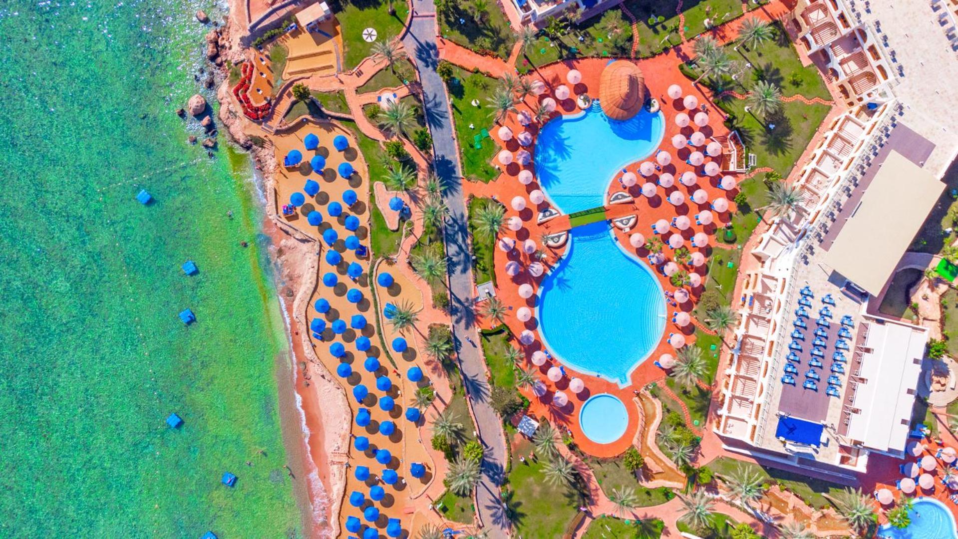 Pickalbatros Royal Grand Sharm - Adults Friendly 16 Years Plus Exteriér fotografie The photo shows an aerial view of a beach resort. In the foreground, there's a large swimming pool shaped like a flowing river, surrounded by lounge chairs and umbrellas. The pool has a distinctive, organic design with curved edges. To the left, ther