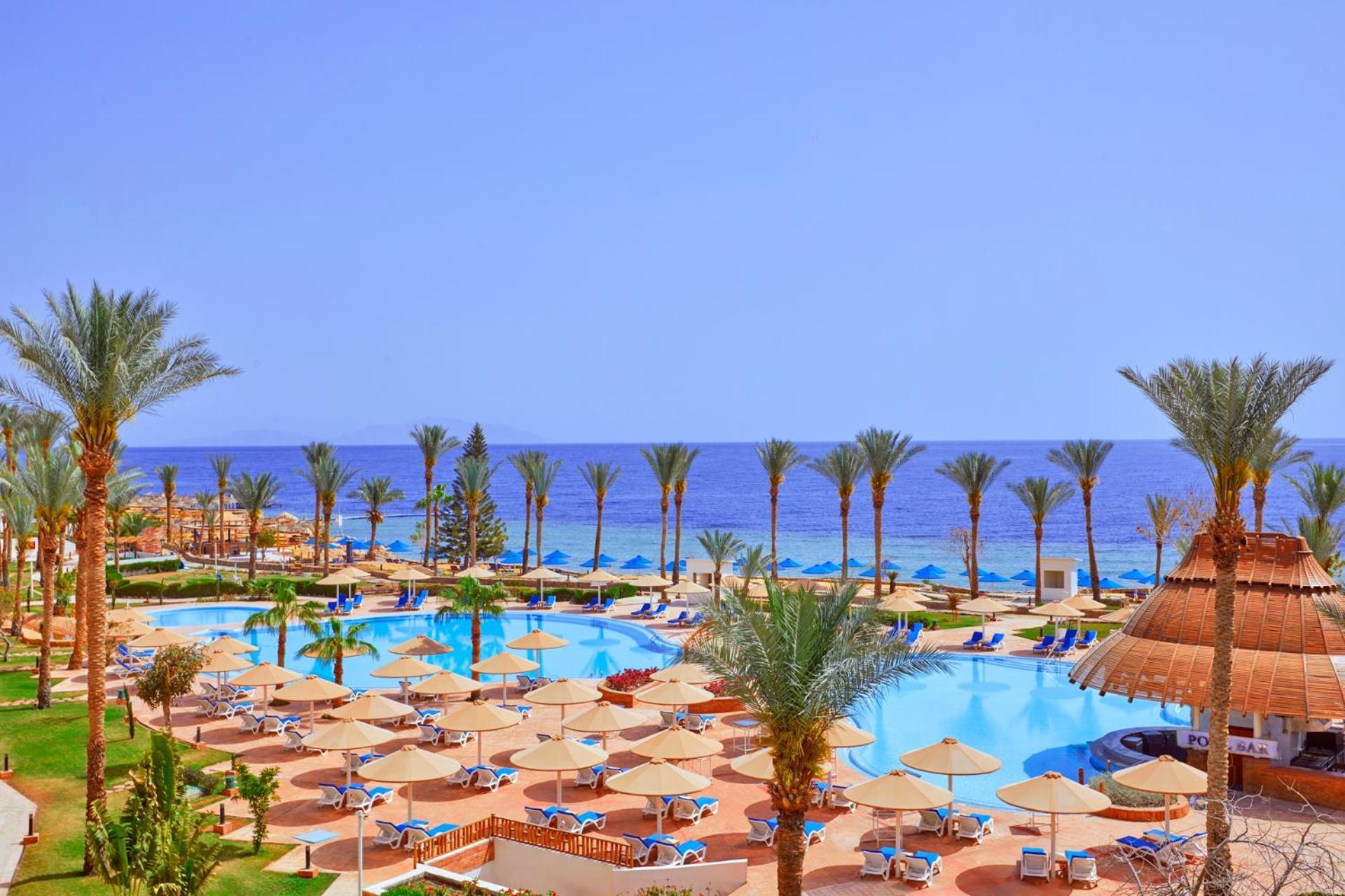 Pickalbatros Royal Grand Sharm - Adults Friendly 16 Years Plus Exteriér fotografie The photo showcases a beautiful resort setting by the sea. It features a large swimming pool surrounded by sunny lounge chairs and umbrellas, perfect for relaxation. The area is adorned with lush palm trees, adding to the tropical vibe. In the backgr