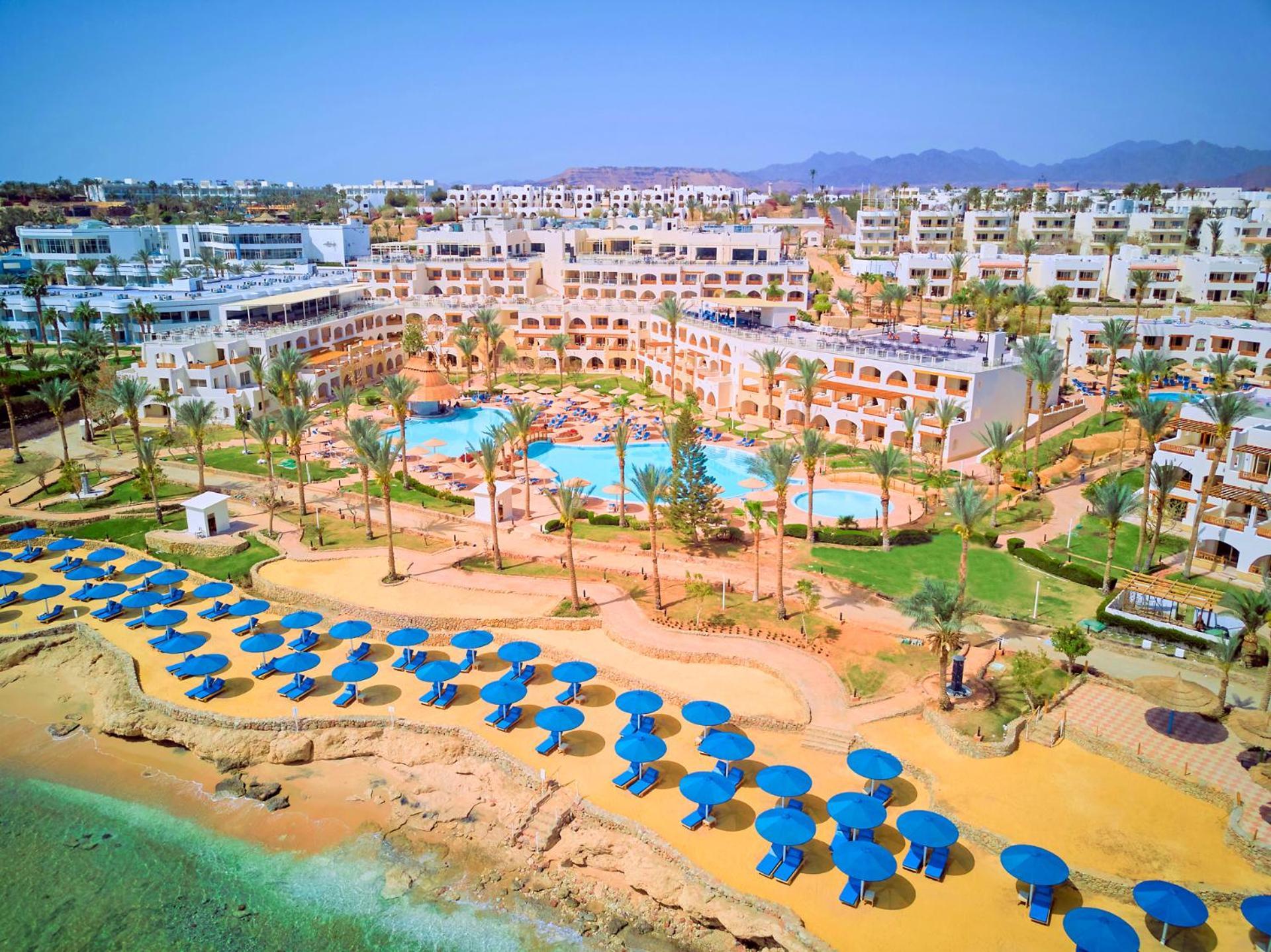 Pickalbatros Royal Grand Sharm - Adults Friendly 16 Years Plus Exteriér fotografie The photo shows a vibrant resort area with several buildings that appear to be accommodations or hotel units. There are multiple swimming pools surrounded by palm trees, creating a tropical atmosphere. In the foreground, there is a beach area with sa