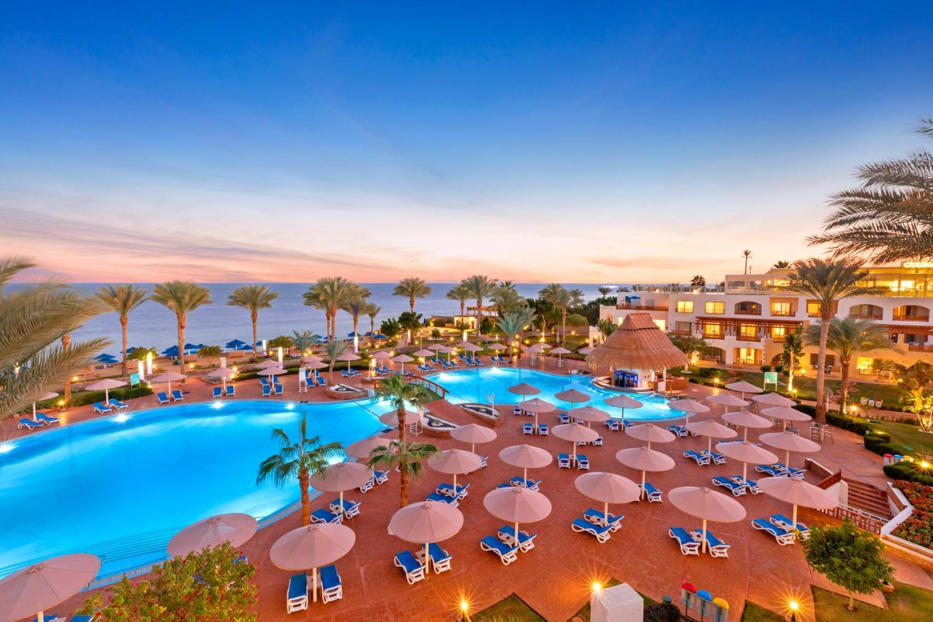 Pickalbatros Royal Grand Sharm - Adults Friendly 16 Years Plus Exteriér fotografie The photo showcases a luxurious resort setting with two large swimming pools, surrounded by lounge chairs and umbrellas. Palm trees are interspersed around the pool area, enhancing the tropical feel. In the background, there’s a view of the ocean, an