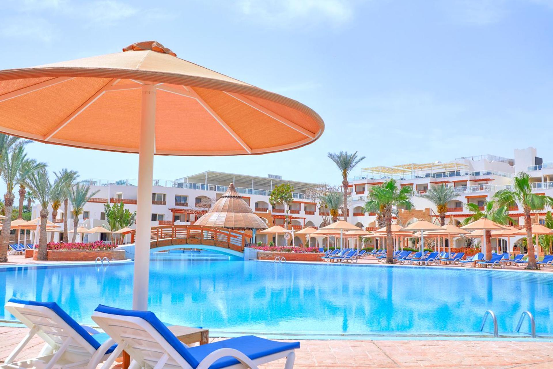 Pickalbatros Royal Grand Sharm - Adults Friendly 16 Years Plus Exteriér fotografie The photo shows a picturesque resort scene featuring a large swimming pool surrounded by lounge chairs and umbrellas. The pool is shimmering under a bright blue sky, and there are several palm trees in the background, adding to the tropical atmospher
