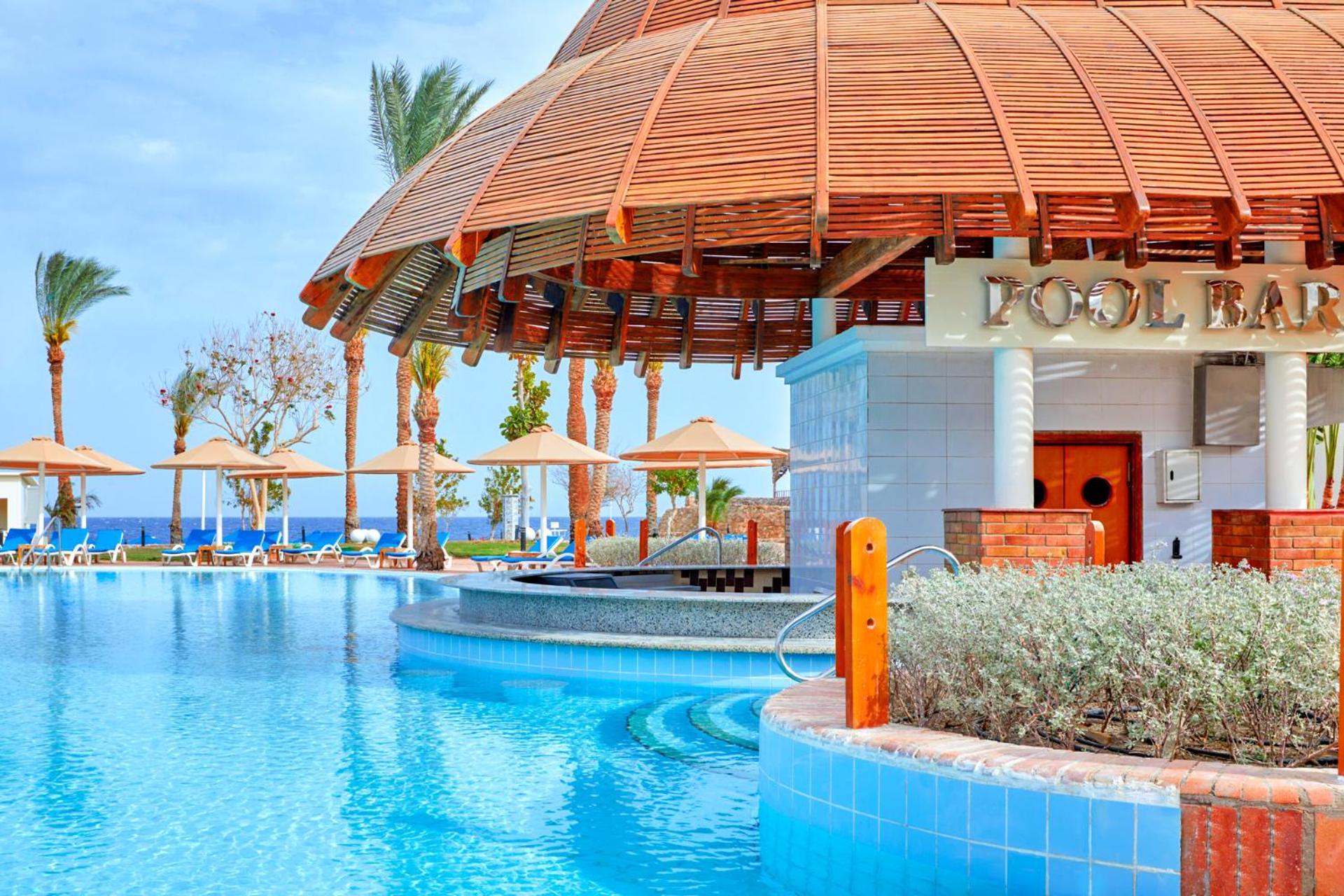 Pickalbatros Royal Grand Sharm - Adults Friendly 16 Years Plus Exteriér fotografie The photo depicts a picturesque pool area at a resort. In the foreground, there is a clear and inviting swimming pool with curved edges, surrounded by a light blue tile border. To the side, a pool bar is visible with a wooden roof and stylish archite
